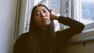 a woman leaning with her head on her hand against a white wall